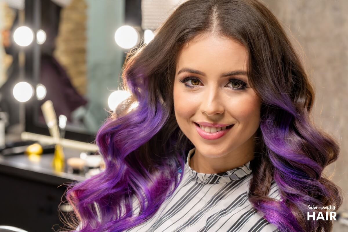 woman showing how purple highlights look on her dark brown hair in a salon